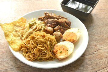 dry boiled Chinese yellow egg noodles with braised beef and meatball dressing black sweet soy sauce topping egg on plate