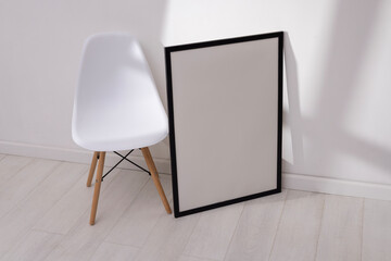 Mockup of empty frame in modern minimalist interior with chair and morning light on white wall background. Template for artwork, painting, photo or poster