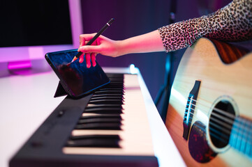 Asian teen girl playing guitar, composing music in home recording studio, LED lighting, at night using computer, headphones, condenser microphone, tablet and keyboard for mixing and mastering music.