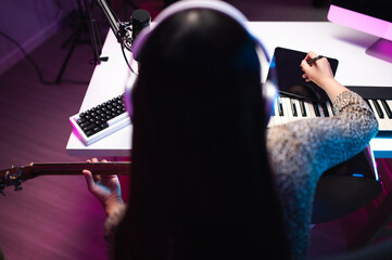 Asian teen girl playing guitar, composing music in home recording studio, LED lighting, at night...