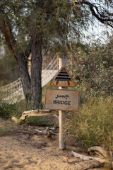 A yellow, bilingual road sign indicates a bridge ahead with an icon of a bridge and a words in both English and Arabic languages. Dubai, Mushrif park, 16.02.25, UAE