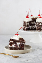 Piece of Black forest cake with cherry, cream with shea butter, cognac and chocolate biscuit and cup of coffee on a white table. Vegan dessert. Vertical orientation.
