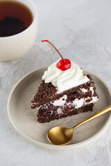 Piece of vegan Black forest cake with cherry, cream with shea butter, cognac and chocolate biscuit and cup of tea. Vertical orientation.
