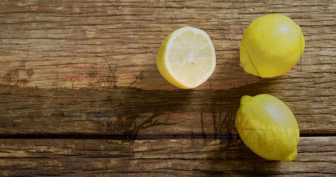 Lemons and lemon half casting soft shadows on rustic wooden surface