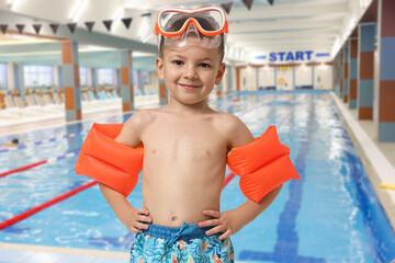 Cute little boy in trunks with diving mask and swim armbands at indoor swimming pool