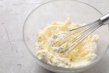 Bowl with whisk and whipped cream on light grey table, closeup