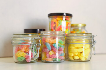 Tasty gummy candies in glass jars on light table, closeup