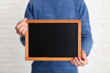 Man holding blank small blackboard indoors, closeup