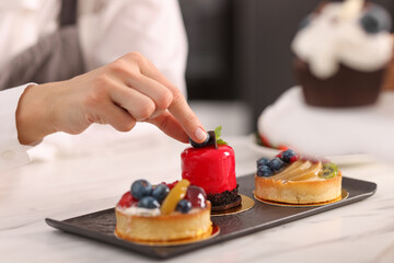 Confectioner decorating delicious dessert with blueberry at table, closeup