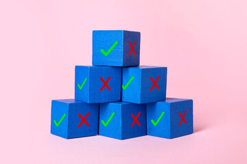 Approve of reject. Pyramid of wooden cubes with check and cross marks on pink background
