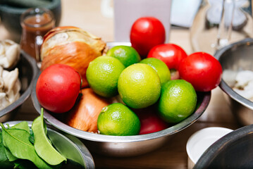 Fresh Limes, Tomatoes and Onions in Bowl. A stainless steel bowl filled with fresh limes, red tomatoes, and onions, ideal for cooking, salads, or food prep.