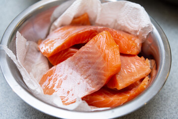 Fresh raw salmon fillets in metal bowl. Close-up of fresh raw salmon fillets placed in a stainless steel bowl with paper towels, ready for cooking or sushi prep.