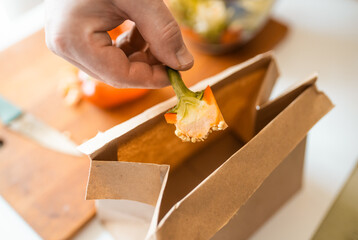  Closeup of hands slicing bell pepper and putting a waste into a paper trash bag. Sustainability concept.