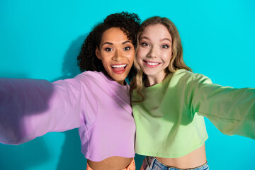 Two young women smiling together for a selfie against a vibrant turquoise background in trendy...