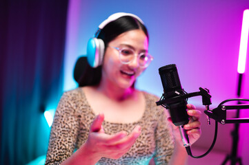 Teenager girl hosts podcast in her room using LED lights, computer, headphones, condenser microphone, tablet to take notes to share knowledge experiences in various fields via live online broadcast.
