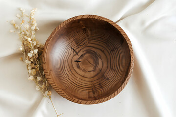 Wooden bowl with concentric rings on white fabric, dried plant beside