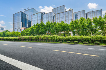 Modern glass office building with green trees and empty road. Urban landscape and transportation background.