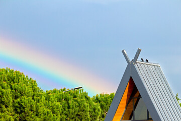 Gable roof hut against rainbow sky background. Rainbow after rain. Calmness, happiness and peace....
