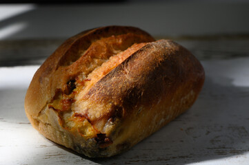 Rustic loaf of freshly baked bread resting on a sunlit wooden table while shadows dance around it
