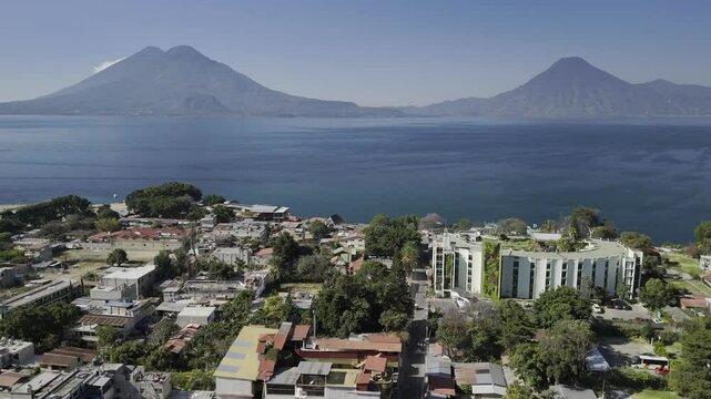 Drone flies over Panajachel, Guatemala to the edge of a serene Lake Atitlan with no boats and two volcanoes on the skyline