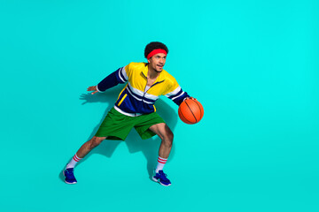 Fototapeta premium Young male basketball player in colorful retro gear dribbling with energy against teal background