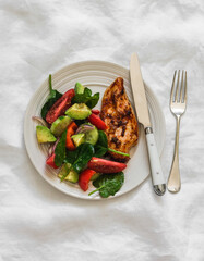 Baked chicken breast and fresh avocado, tomatoes, peppers, spinach salad - a delicious diet lunch on a light background, top view