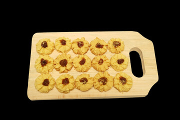 Kue semprit or Butter Cookies is a Traditional Indonesian Cookies, pineapple jam on top for Ied Al Fitr served on Wooden cutting board  and isolated on black background 