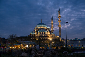 Fototapeta premium Illuminated Yeni Camii Mosque at Night in Eminönü, Istanbul - Historic Ottoman Architecture with Magnificent Domes and Minarets Against Twilight Sky in Turkey