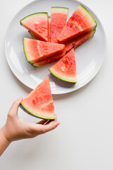 Child hand holding watermelon slice on white plate