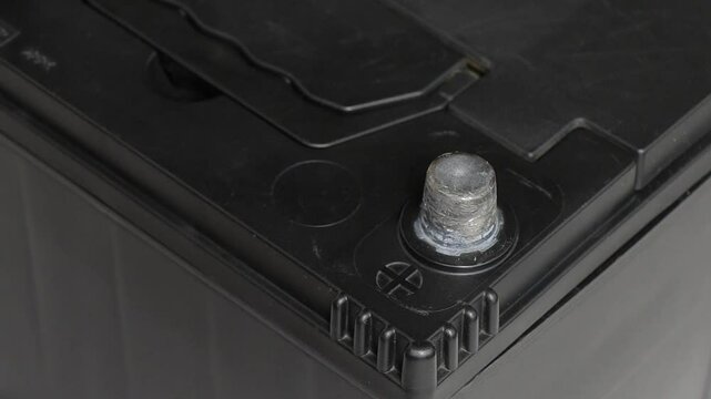 Close-up hand connecting positive terminal of booster cable to car battery. Concept of AGM battery charging and testing.
