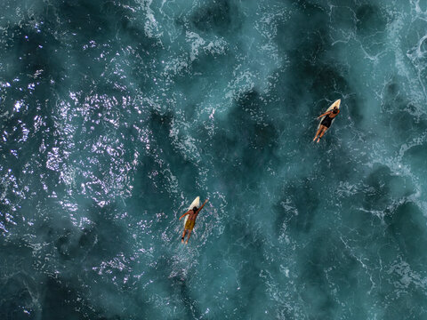 Aerial 90 degree straight down drone photo of a couple - young male and female surfers on a surfboards in the emerald ocean water. Pacific Coast, El Tunco, El Salvador, Central America.