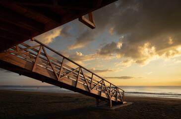 Wooden lifeguard tower overlooking sandy beach at sunrise with cloudy sky