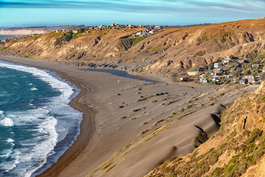 Beautiful beach houses along the coastline of Matanzas in the O'Higgins region of Chile with waves crashing on the sandy shore