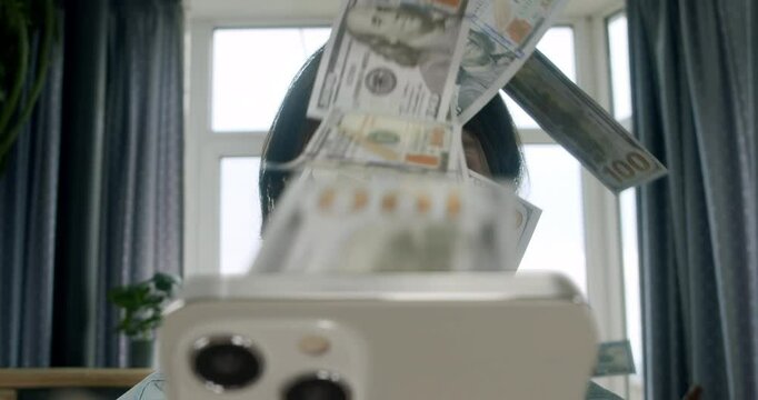 Man earning money online as dollar bills float to his face while using a smartphone. Online business, digital success, and easy earnings. Investor earning money, investments with money rain concept 