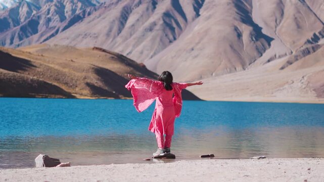 Indian girl wearing salwar suit standing at Chandrataal lake and raising arms. Beautiful high altitude lake in Spiti Valley, India. Tourist enjoying holidays. 