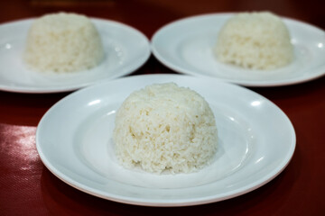 Three servings of white steamed rice, molded into small domes, on white plates. Simple meal staple.
