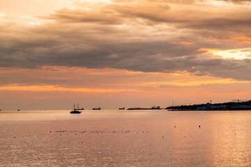 A beautiful sunset over the ocean with a boat in the water. The sky is filled with clouds and the water is calm