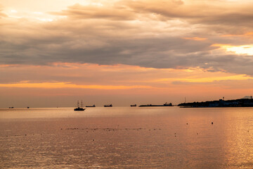 A beautiful sunset over the ocean with a boat in the water. The sky is filled with clouds and the water is calm