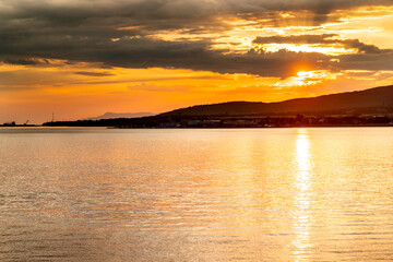 The sun is setting over the water, creating a beautiful orange and pink sky. The water is calm and still, reflecting the colors of the sky. The scene is peaceful and serene