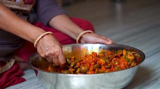 Close up shot of Indian woman making traditional mango pickle at home. Indian woman wearing bangles in hands and mixing spices in pickle. Female preparing food in kitchen. An Indian housewife.