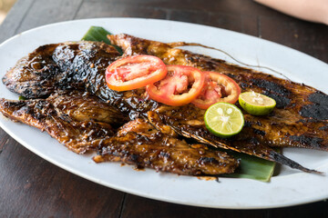 Grilled fish (ikan bakar) served with two chili sauces (sambal) on a green plate. Indonesian seafood dish