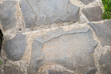 Irregular gray stone slabs form a textured pathway with hints of green moss or grass. Natural and weathered surface.
