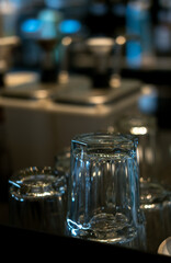 Several clear, empty glasses with a textured base sit upside down on a dark, reflective surface. Awaiting use in a dim setting.
