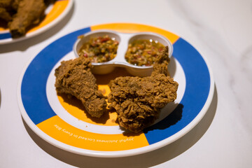 Crispy fried chicken pieces on a colorful plate with two small containers of dipping sauce. A tempting and savory meal.