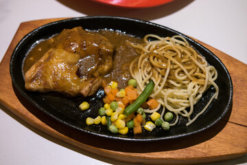 Sizzling plate of chicken steak with brown sauce, spaghetti, and mixed vegetables. A hearty and flavorful meal.