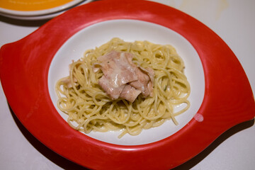 Creamy spaghetti with tuna in a vibrant red bowl. Simple, comforting, and appetizing.