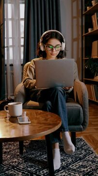 Jeune femme concentr&eacute;e travaillant sur son ordinateur portable avec casque audio dans un salon chaleureux, tasse de caf&eacute; et smartphone pos&eacute;s, chat noir endormi &agrave; ses pieds