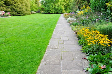 Stone paved path in a beautiful garden with a grass lawn and colourful flowers