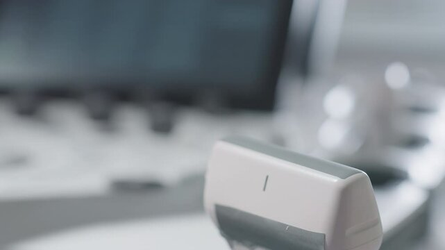 Female lab technologist gloved hands preparing ultrasound transducer by carefully applying gel before beginning patient scan with diagnostic machine blurred in background in clinical environment
