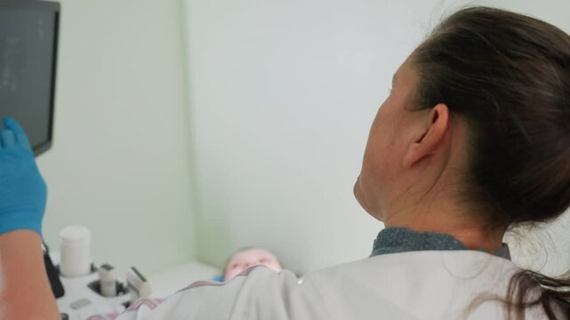 lab scientist explains diagnostic result on monitor to patient lying on bed while both focus on display showing ultrasound data in clinical room with scanning machine and examination tools